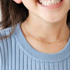 Close-up of a child wearing a blue ribbed sweater with white stripes and a gold necklace.