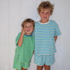 Two children wearing matching green and blue striped outfits standing in front of a white door.