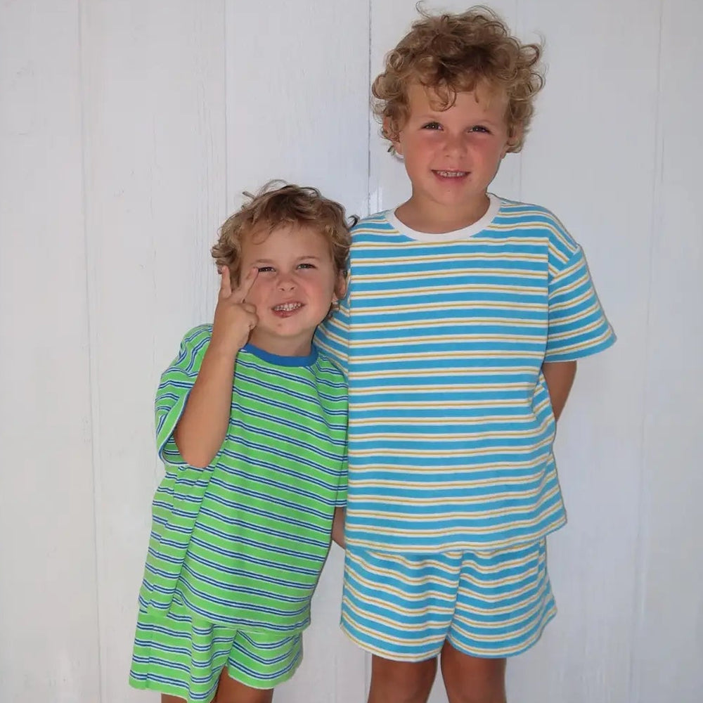 Two children wearing matching green and blue striped outfits standing in front of a white door.