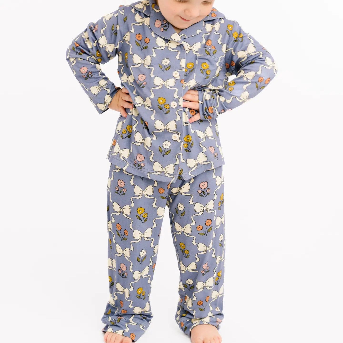 Child wearing a blue pajama set with floral and bow pattern on a white background